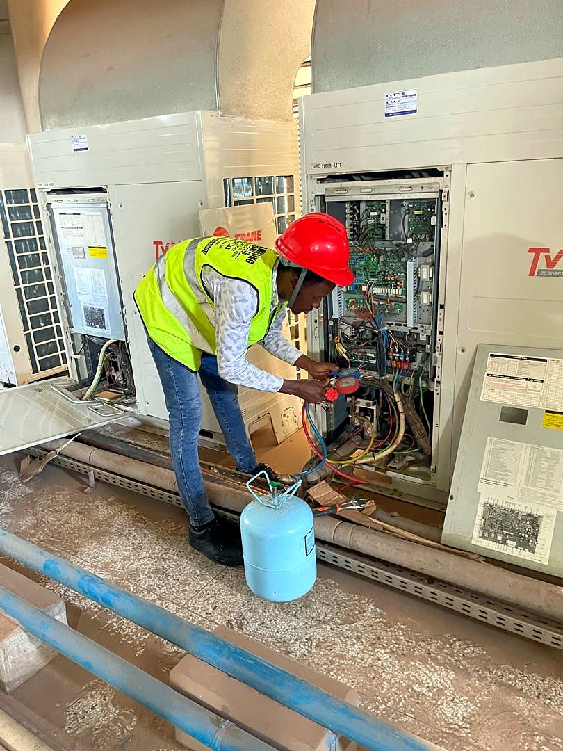 Technician in hi-vis servicing an air-conditioning system with a refrigerant cylinder