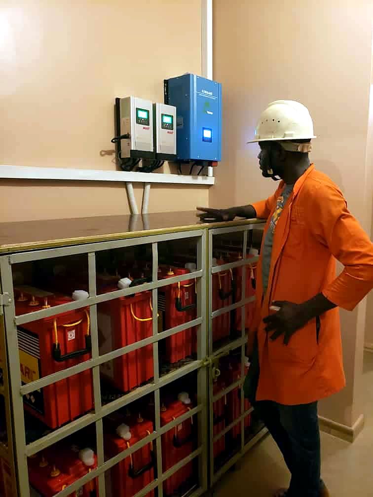 Technician beside a battery bank on shelving with wall-mounted inverters